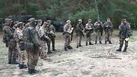 Soldaten stehen in einem Waldgebiet um ihren Vorgesetzten herum. Er erläutert die Lage.