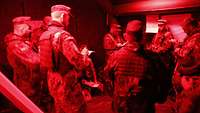 In einem Zelt mit Rotlicht stehen ein Vorgesetzter vor Soldaten und erteilt Befehle..