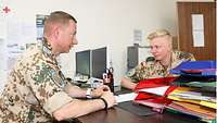 Zwei Soldaten sitzen sich an einem Schreibtisch gegenüber und besprechen ein darauf liegendes Dokument