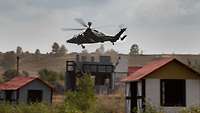 Ein Hubschrauber fliegt über ein Übungsdorf mit Häusern und angedeuteten Mauern.