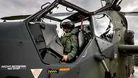 Blick in ein geöffnetes Cockpit eines Hubschraubers. Darin sitzt ein Pilot mit einem Helm.