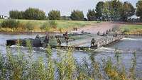 Soldaten bauen eine Brücke aus Pontons zusammen. Sie ragt bereits bis zur Hälfte über den Fluss.