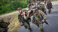 Vier Soldaten tragen eine Behelfstrage mit Gepäck und laufen dabei schnell.