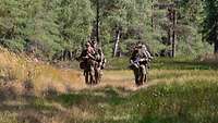 Mehrere Soldaten marschieren durch ein Waldstück.