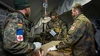 In einem Rettungszelt versorgen zwei Sanitäter einen Verletzten, ein Soldat übermittelt Infos.