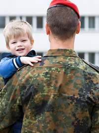 Ein Soldat hält seinen Sohn auf dem Arm, im Hintergrund angetretene Soldaten