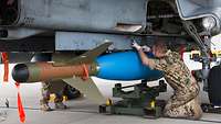 Techniker unter einem Kampfjet mit Bombe