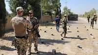 Zwei Soldaten unterhalten sich. Im Hintergrund laufen weitere afghanische Soldaten auf unbefestigtem Gelände