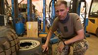 Ein Soldat kniet neben einem ausrangierten Reifen in einer Werkstatt 