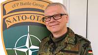 Matthias O. steht vor einem Gebäude. Hinter ihm ist das Wappen der EFP Battle Group NATO zu lesen