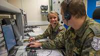 Julia Becher und ein weiteer Soldat sitzen mit Headsets an ihren Computern.