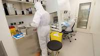 Person in weißem Schutzanzug arbeitet in einem Laborraum