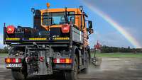 Über einer großen Kehrmaschine der Bundeswehr teilt ein Regenbogen den Himmel in eine blaue und eine graue Hälfte.