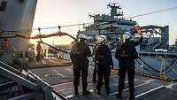 Auf dem Oberdeck eines Schiffes steht eine Gruppe von fünf Marinesoldaten in blauer Arbeitsuniform und mit Schutzhelmen.