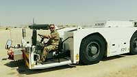 Ein Soldat sitzt im hinteren Fahrstand des Schleppfahrzeuges und seht auf einem Flugfeld