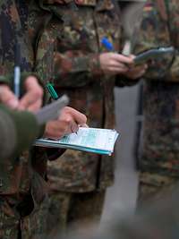 Mehrere Soldaten stehen mit Schreibblöcken und Stiften im Halbkreis und schreiben.