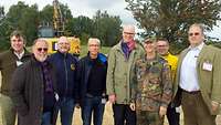 Gruppenbild mit etwa zehn zivil gekleideten Personen und einem Soldaten.