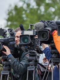 Journalisten stehen mit ihren Kameras und ihren Stativen nebeneinander. Alle Objektive schauen in eine Richtung.