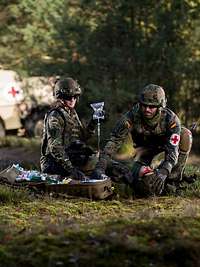 Zwei Sanitäter versorgen einen am Boden liegenden Verwundeten