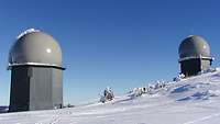 Die zwei Gebäude der Radarstation "Großer Arber" im Winter, bei blauem Himmel und Schnee.