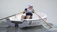 Ein CISM-Sportler rudert rückwärts sitzend in einem Boot und blickt in Fahrtrichtung.