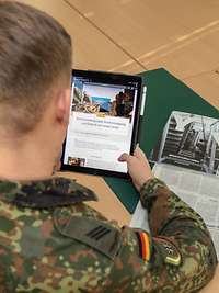 Ein Soldat sitzt an einem Tisch mit Zeitschriften und hält ein Tablet in der Hand.