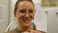 Kathrin G. steht in einem Behandlungsraum und hält eine Spritze in ihrer Hand