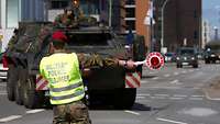 Ein Soldat mit einer Verkehrskelle leitet ein Bundeswehrfahrzeug nach rechts.