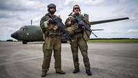 Zwei bewaffnete Soldaten stehen auf einem Flugfeld.