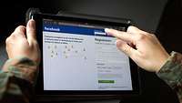 Soldat hält ein Tablet mit der Anmeldeseite von Facebook in der Hand
