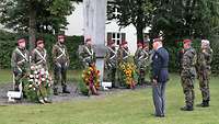 Mehrere Soldaten stehen an einem Denkmal vor und hinter Kränzen.