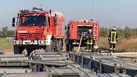 Zwei Feuerlöschfahrzeuge Waldbrandbekämpfung stehen auf dem Testgelände in Meppen, davor viele Metallkisten.