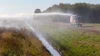 Ein Waldbrandlöschfahrzeug sprüht von einem Weg aus mit seinem Dachwerfer Wasser auf den Moorbrand in Meppen. 