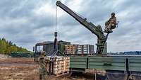 Ein Soldat entlädt von einer Krananlage eines Lkw aus Paletten mit Munition.