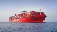 Ein großes Containerschiff mit rotem Rumpf auf See.