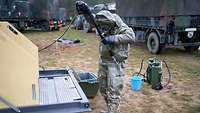Ein Soldat reinigt seinen Schutzanzug mit dem Hochdruckreiniger