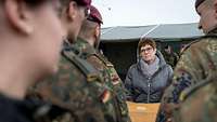 Eine Frau in einer grauen Winterjacke hört Soldaten zu, die vor ihr stehen und reden.