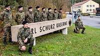 Zehn Soldaten hocken und stehen rund um den Schriftzug „Carl Schurz Kaserne“ vor dem Kasernentor.