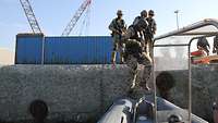 Vier bewaffnete Soldaten steigen von der Pier in ein Schlauchboot