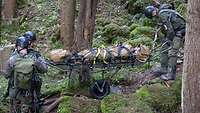 Drei Soldaten transportieren einen Verletzten mit einer speziellen Trage mit Fahrgestell einen schweren Bergweg hinunter.