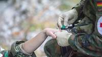 Ein Soldat legt mit einer Nadel einen Zugang an der Oberseite der Hand.