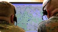 Zwei Soldaten mit Headset blicken in einen Computerbildschirm, der eine taktische Lagekarte zeigt.