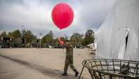 Ein Soldat mit einem roten Wetterballon in der Hand