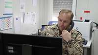 Ein deutscher Soldat im Einsatz sitzt in seinem Büro und telefoniert während er auf einen Computerbildschirm schaut