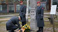 Zwei Soldaten stehen neben dem Stauffenberg-Gedenkstein, ein Soldat legt einen Kranz davor nieder.