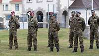 Ein Gruppe Soldaten steht mit Abstand in zwei Reihen auf einer Wiese. Alle tragen Masken und verschiedene Kopfbedeckungen.