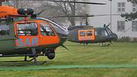 Zwei Hubschrauber stehen leicht versetzt hintereinander auf einer Wiese.