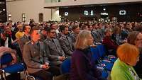 Soldaten sitzen in einem Saal inmitten ziviler Zuhörer.