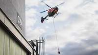 Ein Hubschrauber schwebt neben einer Werkshalle in der Luft.