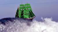 Ein dreimastiges Segelschiff mit grünen Segeln auf, der Rumpf fast vollständig von einer Welle verdeckt.